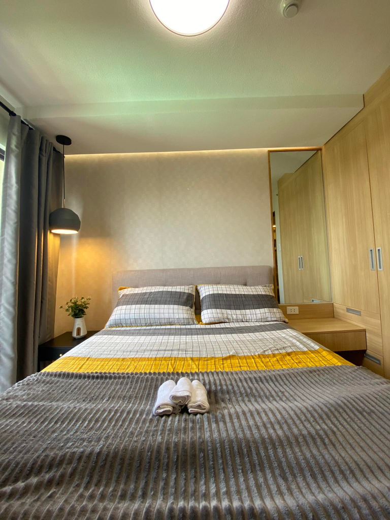 A well-appointed bedroom in a 2-bedroom unit, showcasing a comfortable bed with stylish bedding and a modern pendant light. The room is tastefully decorated and feels spacious.