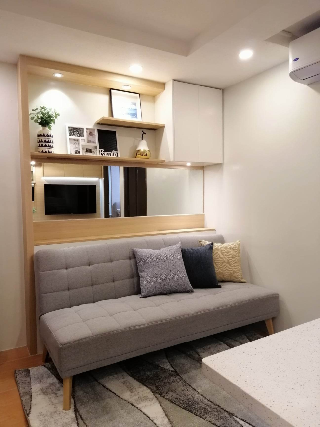 The living area of a 2-bedroom unit, featuring a comfortable sofa with built-in shelving and a mirrored wall, creating a spacious and stylish atmosphere.