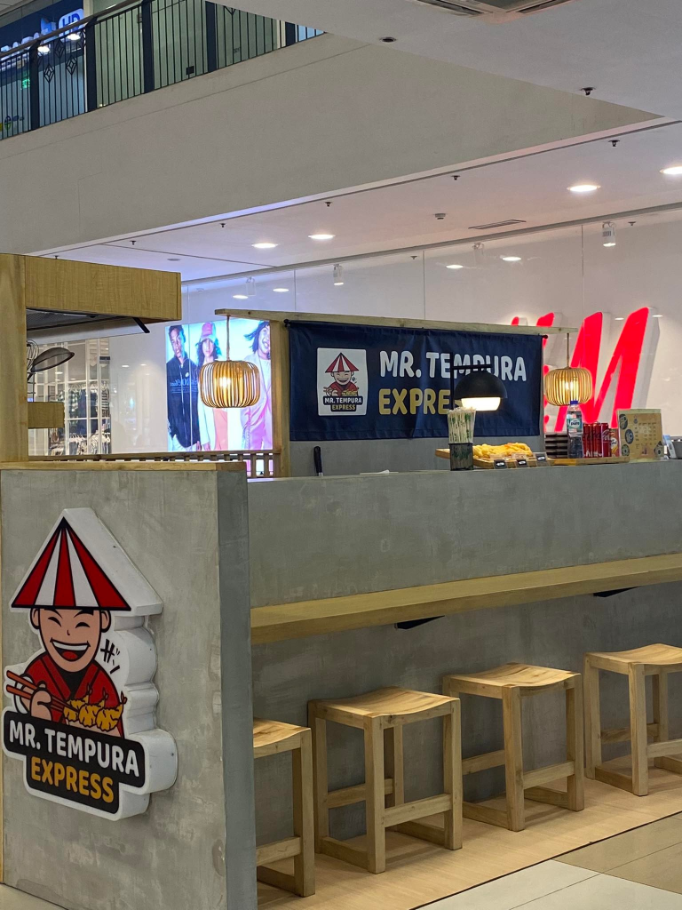 Mr. Tempura Express food stall showcases a minimalist and modern design with a clean, grey counter and wooden accents. The image highlights the stall's branding and efficient layout within a shopping mall environment.