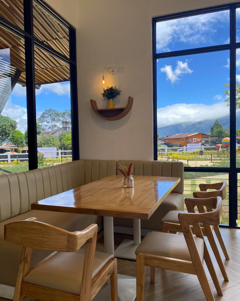 Skye 88 Cafe features a comfortable seating area with wooden tables and chairs, offering stunning views of the surrounding landscape through large windows. The design is modern and inviting.
