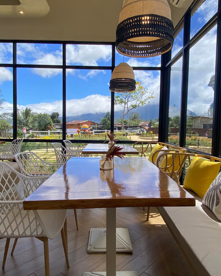 Skye 88 Cafe offers a unique dining experience with its stunning views. This image showcases the cafe's interior seating area, featuring wooden tables and chairs, with large windows providing a picturesque view of the surrounding landscape and mountains.