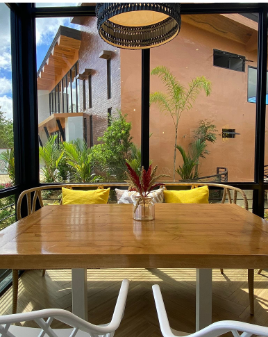 Skye 88 Cafe offers a unique dining experience. This image showcases a cozy seating area with a large wooden table and comfortable chairs, situated near a window offering a view of the surrounding buildings and lush greenery.