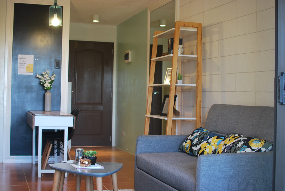 The living area of a cozy and well-furnished 1-bedroom unit, showcasing a comfortable sofa, a stylish bookshelf, and a small dining area. The image highlights the unit's functional and aesthetically pleasing design.