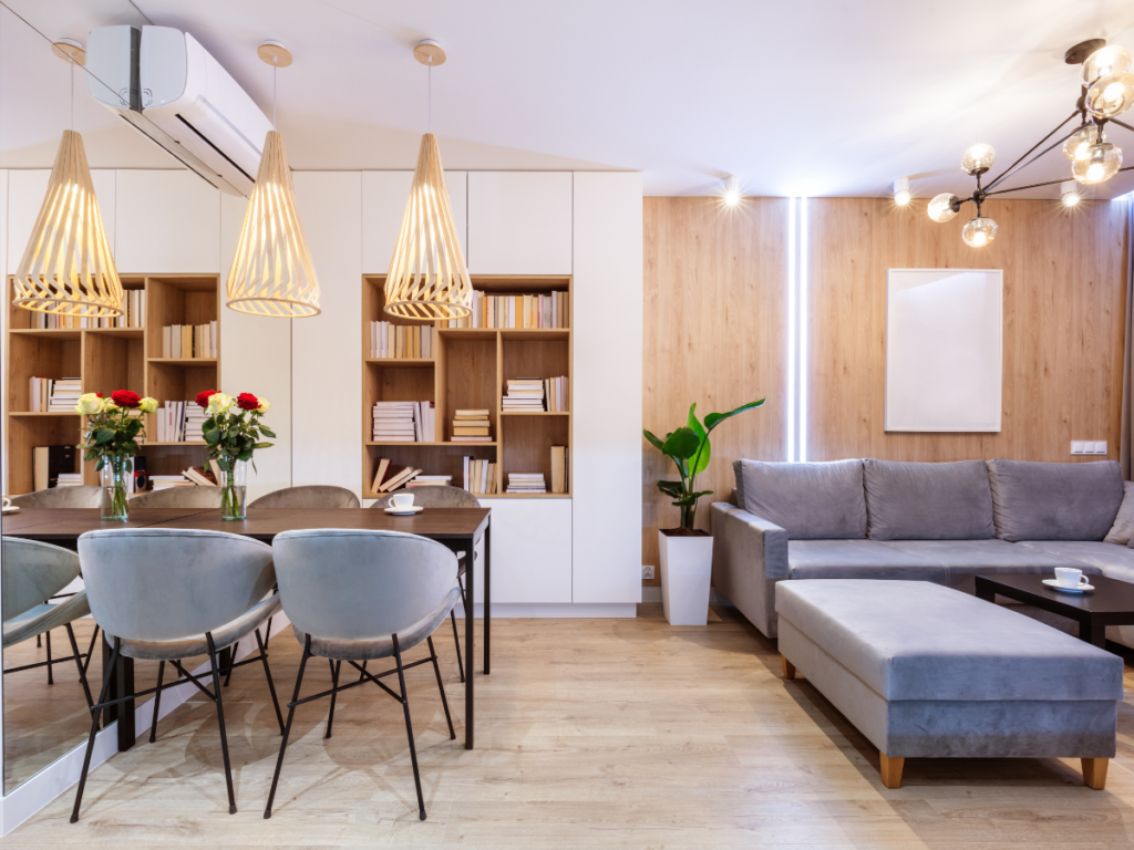 A small apartment living room features a light and airy design. A built-in shelving unit maximizes storage, while a compact sofa and dining set create a functional and stylish space. The use of light colors and vertical shelving visually expands the room.