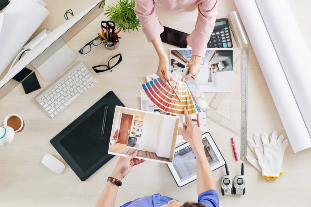 Overhead view of a design consultation, showing various design elements such as color palettes, floor plans, and digital tools spread across a table. This illustrates a comprehensive design planning session.